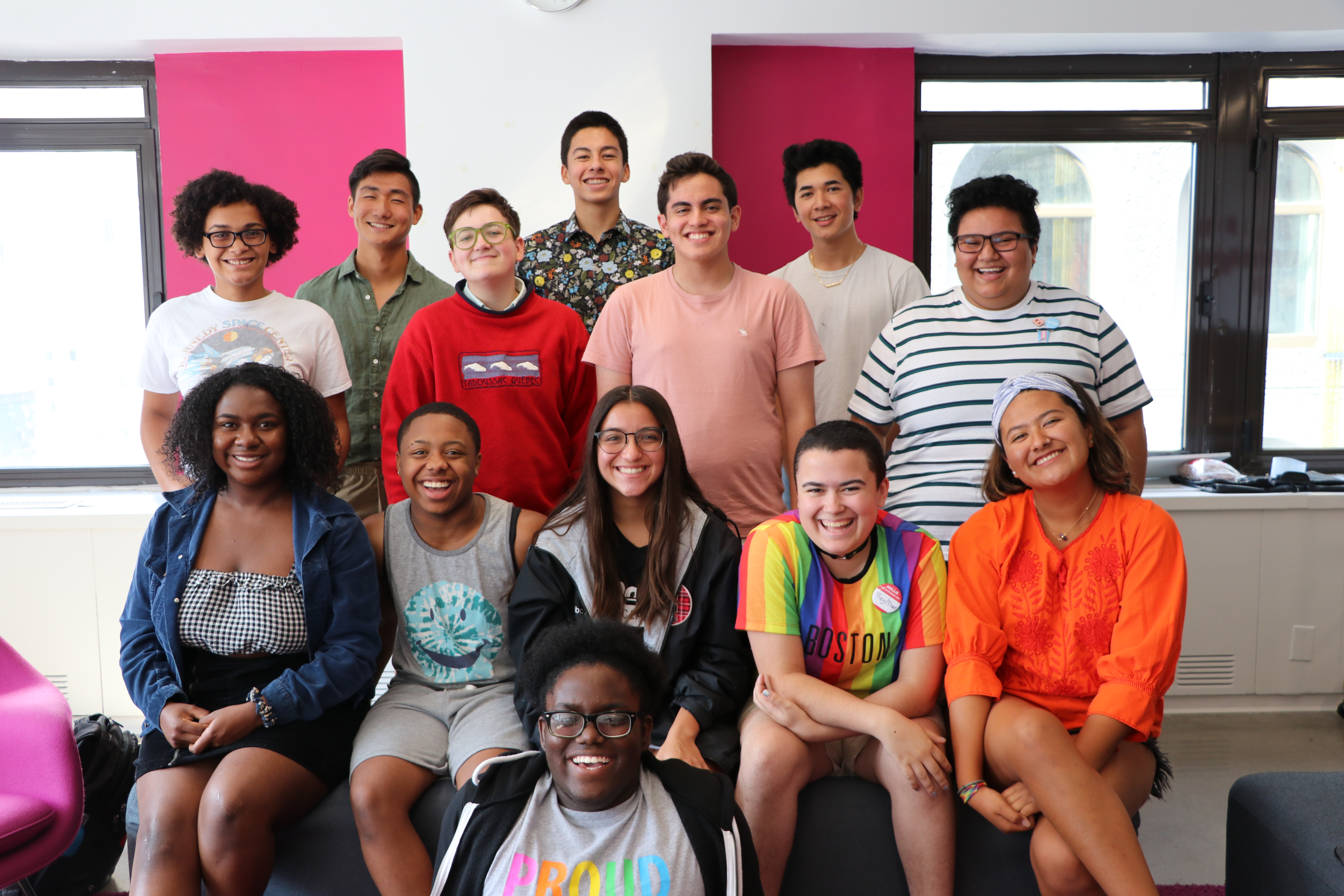 Group of students in a group smiling at the camera. Half are standing, others are sitting, one is sitting on the ground. 